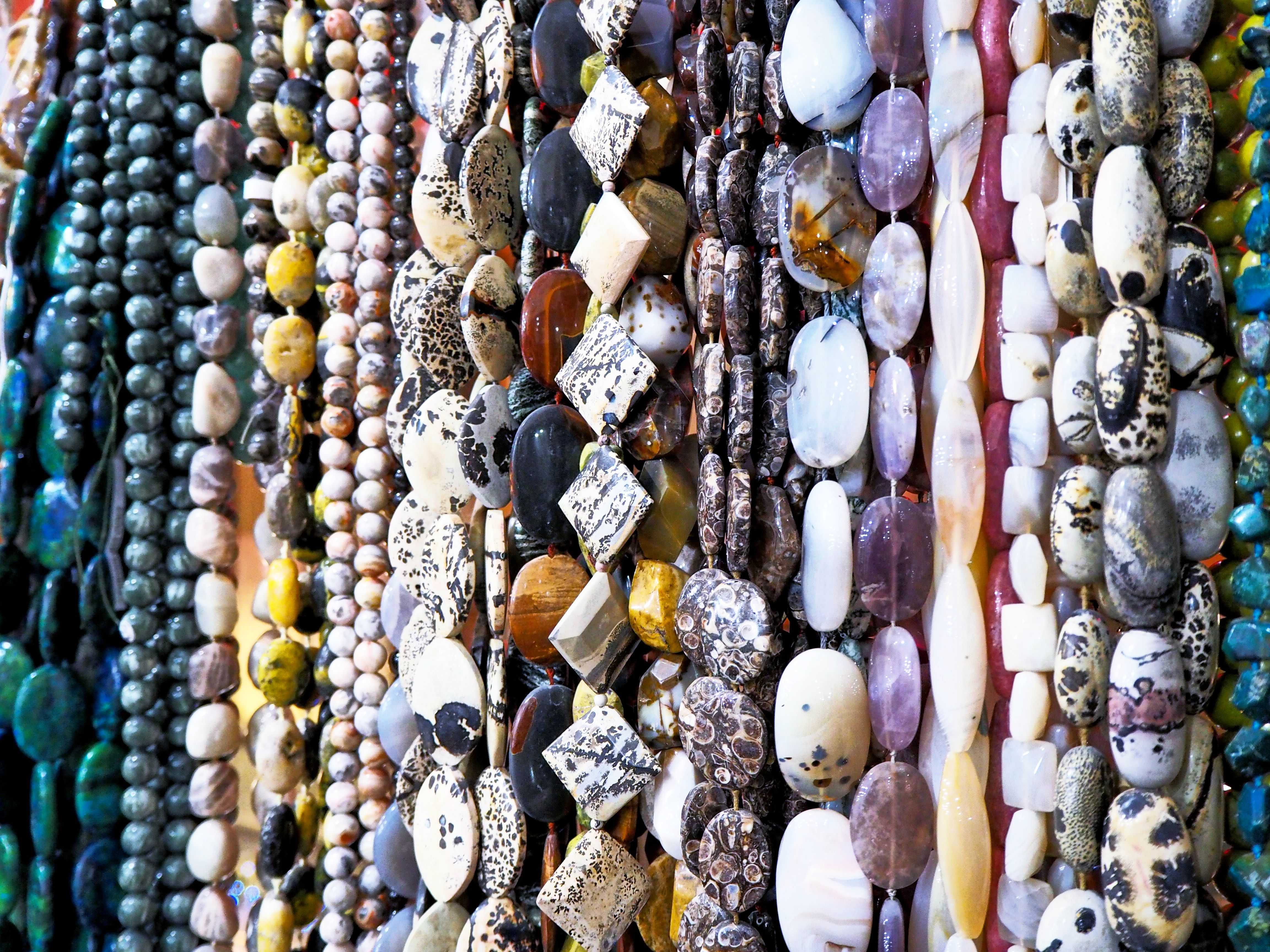Rangée de nombreux fils de perles en pierres et minéraux colorés suspendus verticalement, motifs et teintes variées créant une ambiance chaleureuse et minérale